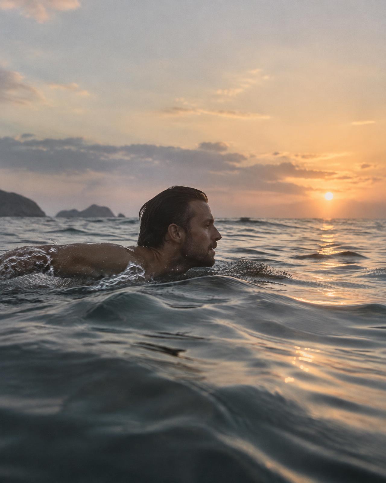A man swimming in open water at sunrise
